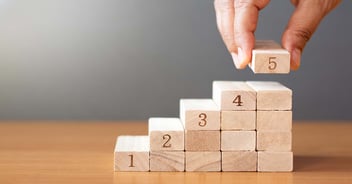 businessperson stacking blocks with numbers one through five